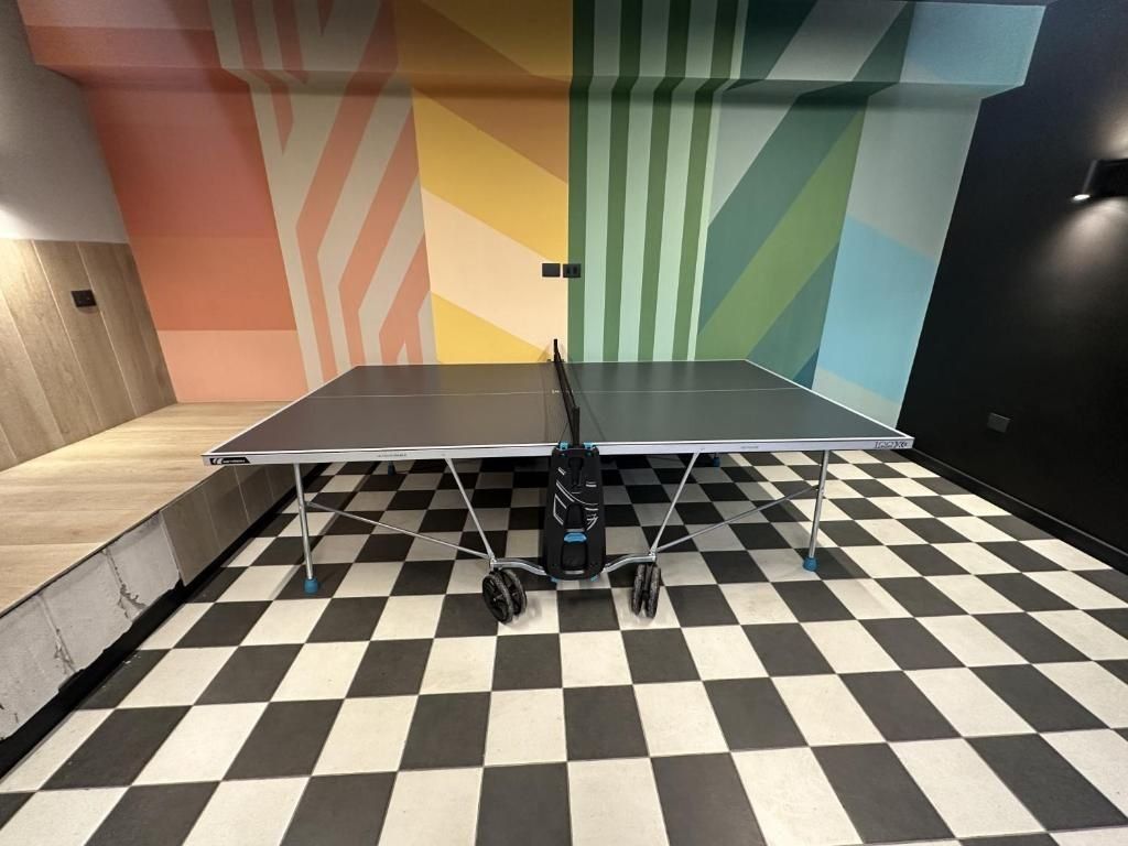 Een tafeltennistafel in een ruimte met een geruit vloertapijt en kleurrijke muurmotieven.