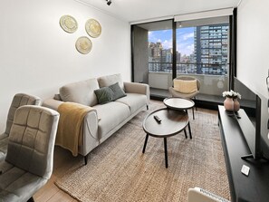 Una sala moderna con un sofá, sillones, una mesa de centro y vistas a la ciudad a través de amplios ventanales.