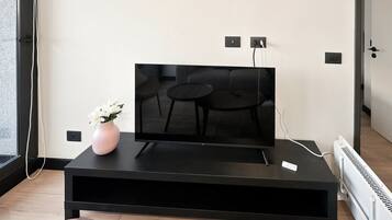Un soggiorno moderno con una TV a schermo piatto su un mobile nero, un vaso con fiori bianchi e un termosifone bianco.