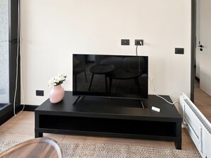 Un salon moderne avec un téléviseur à écran plat posé sur un meuble noir, un vase avec des fleurs blanches et un radiateur blanc.