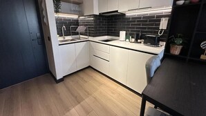 A modern kitchen with white cabinets, a black tiled backsplash, and a wooden floor. - Oceana Suites San Eugenio (Santiago)