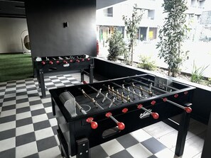 Two foosball tables in a room with a checkered floor and a view of buildings outside. - Oceana Suites San Eugenio (Santiago)
