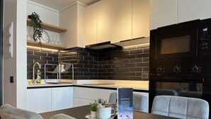 A modern kitchen with black tiled backsplash, stainless steel appliances, and a dining area with a table and chairs. - Oceana Suites San Eugenio (Santiago)