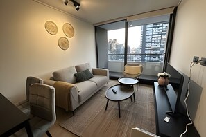 A modern living room with a sofa, a coffee table, and a view of a cityscape through large windows.