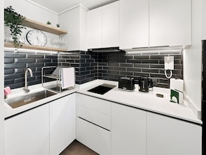 A modern kitchen with white cabinets, a black backsplash, and a stainless steel sink.