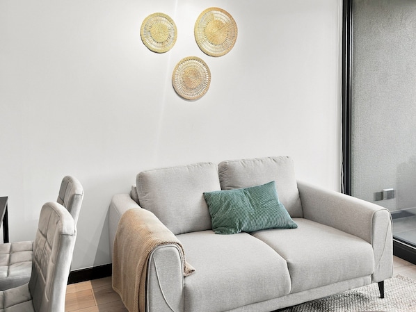 A modern living room with a grey sofa, a green pillow, and a beige throw blanket.