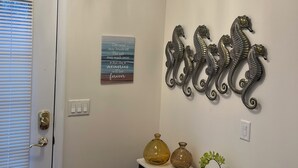 A hallway with a chandelier, decorative metal seahorses, a sign, and a small table with vases. - The LemonDrop: 3-bedroom townhome in charming Lewes minutes away from Beaches! (Lewes)