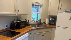 A kitchen with white cabinets, a wooden countertop, a dishwasher, a refrigerator, and a window with blinds. - Charming tiny house in the mountains on a goat farm in Murphy, NC (Murphy)