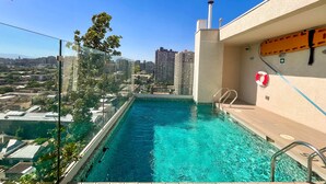 Ein Pool auf dem Dach mit klarem, blauem Wasser, umgeben von einer Glasbarriere und mit Blick auf eine Stadtlandschaft.