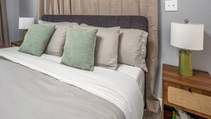 Un letto rifatto con lenzuola bianche e cuscini verdi, una testiera grigia e due comodini con lampade.