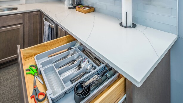 Una cucina con un piano di lavoro bianco, un cassetto con utensili e una macchina per il caffè.