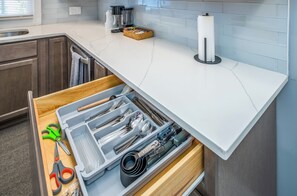 Eine Küche mit weißer Arbeitsplatte, einer Schublade voller Kochutensilien und einer Kaffeemaschine.