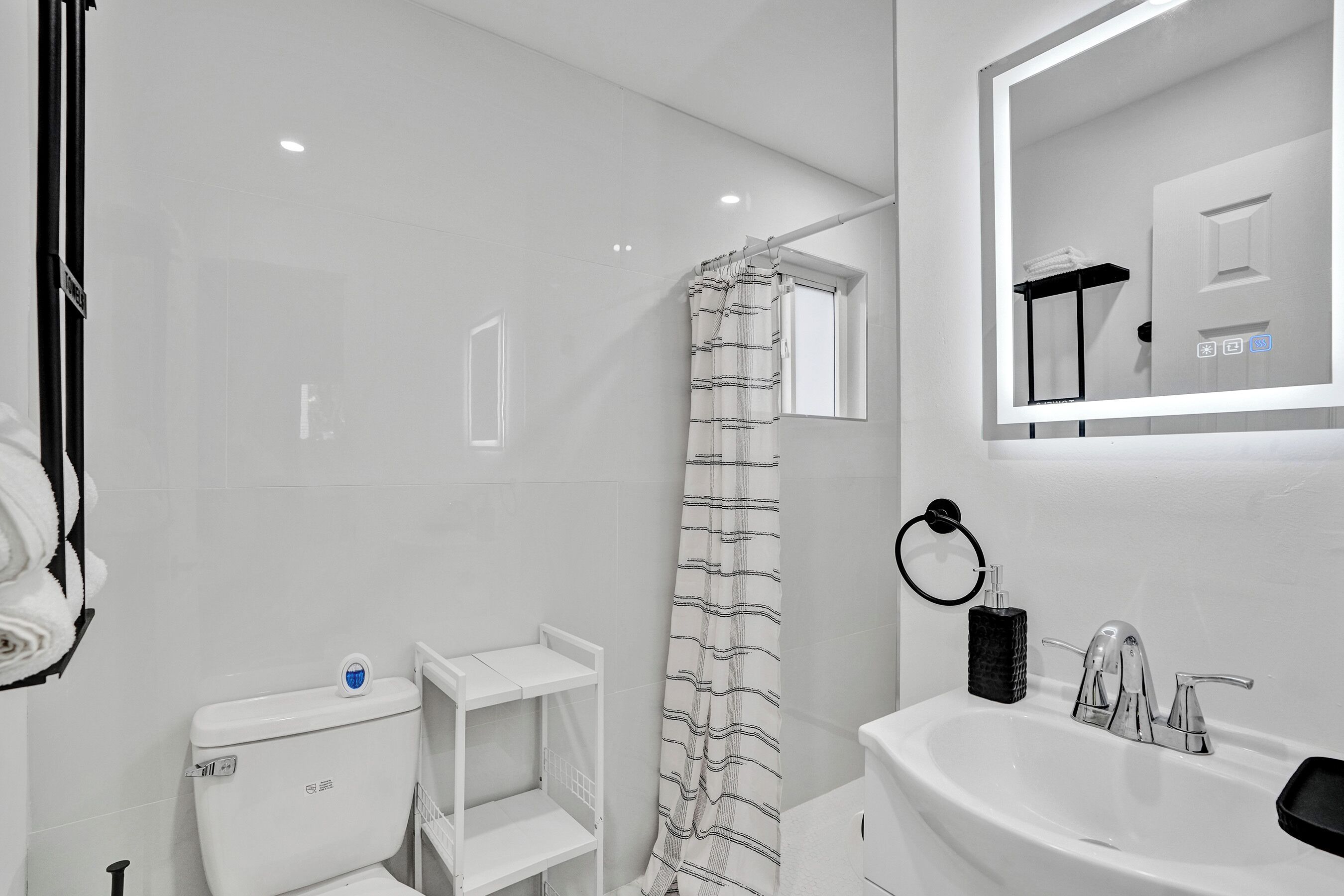 A modern bathroom with a white toilet, a shower with a striped curtain, a sink with a mirror above it, and a towel rack.