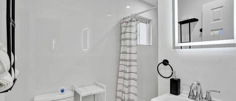 A modern bathroom with a white toilet, a shower with a striped curtain, a sink with a mirror above it, and a towel rack.