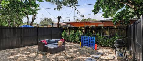 A backyard with a patio area, a grill, and a fenced garden.