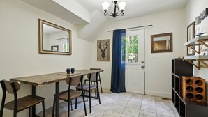 Un comedor con mesa y sillas de madera, una araña y una obra de arte con cabeza de ciervo en la pared.