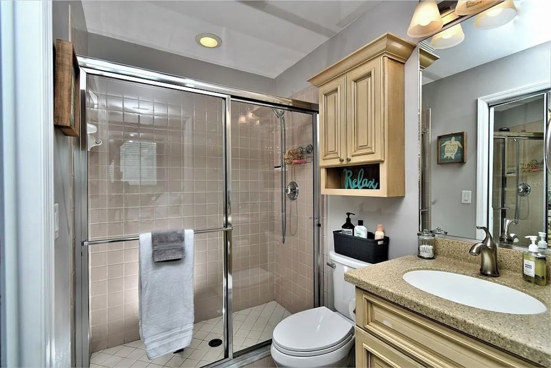 A modern bathroom with a glass-enclosed shower, a white toilet, a vanity with a sink, and wooden cabinets.