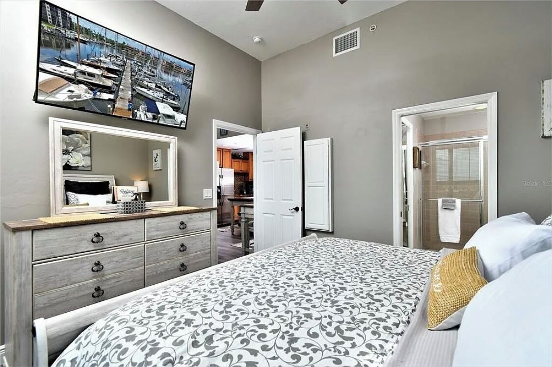 Une chambre à coucher comprenant un lit, une commode, un miroir, un téléviseur et une porte donnant sur une salle de bain.