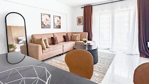 Un salon moderne avec un canapé beige, une table basse ronde et un coin repas comprenant une table noire et des chaises aux motifs géométriques.