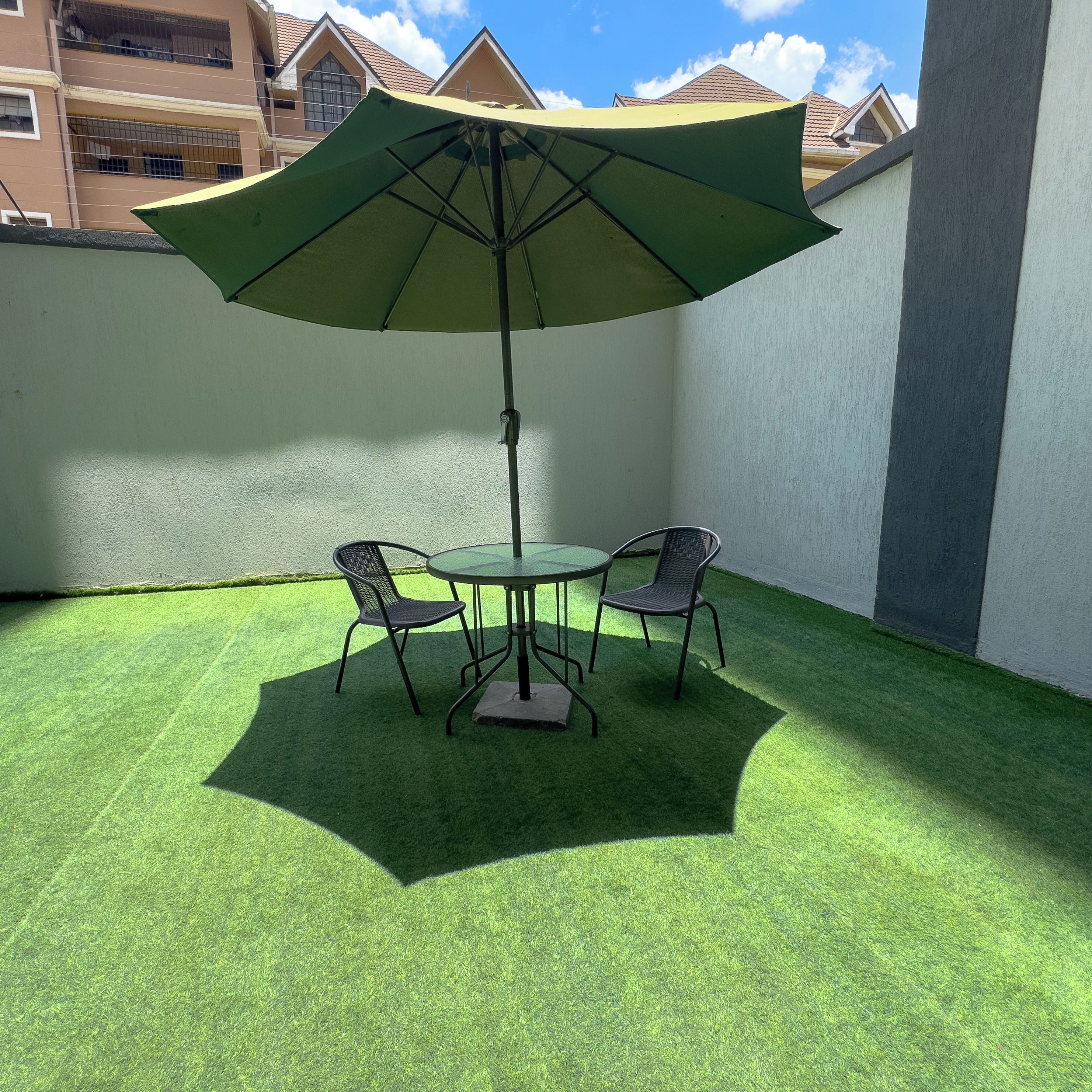 A patio with artificial grass, a table, two chairs, and a large umbrella.