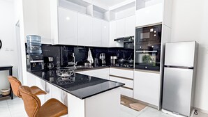 Een moderne keuken met witte kasten, een zwart aanrecht en roestvrijstalen apparatuur, en twee barkrukken.