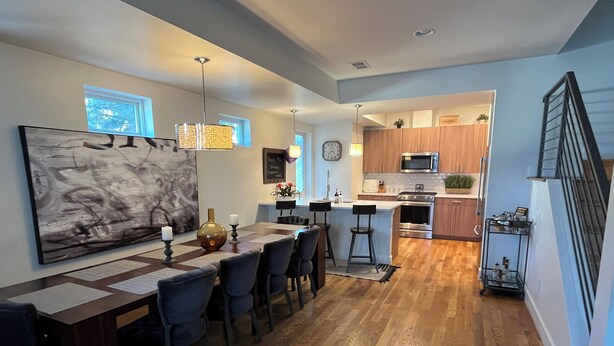 A modern kitchen with wooden cabinets, a central island, and a dining area with a large abstract painting. - Downtown rooftop, hot tub retreat adjacent to RiNo & Lodo Walk score of 95! (Denver)