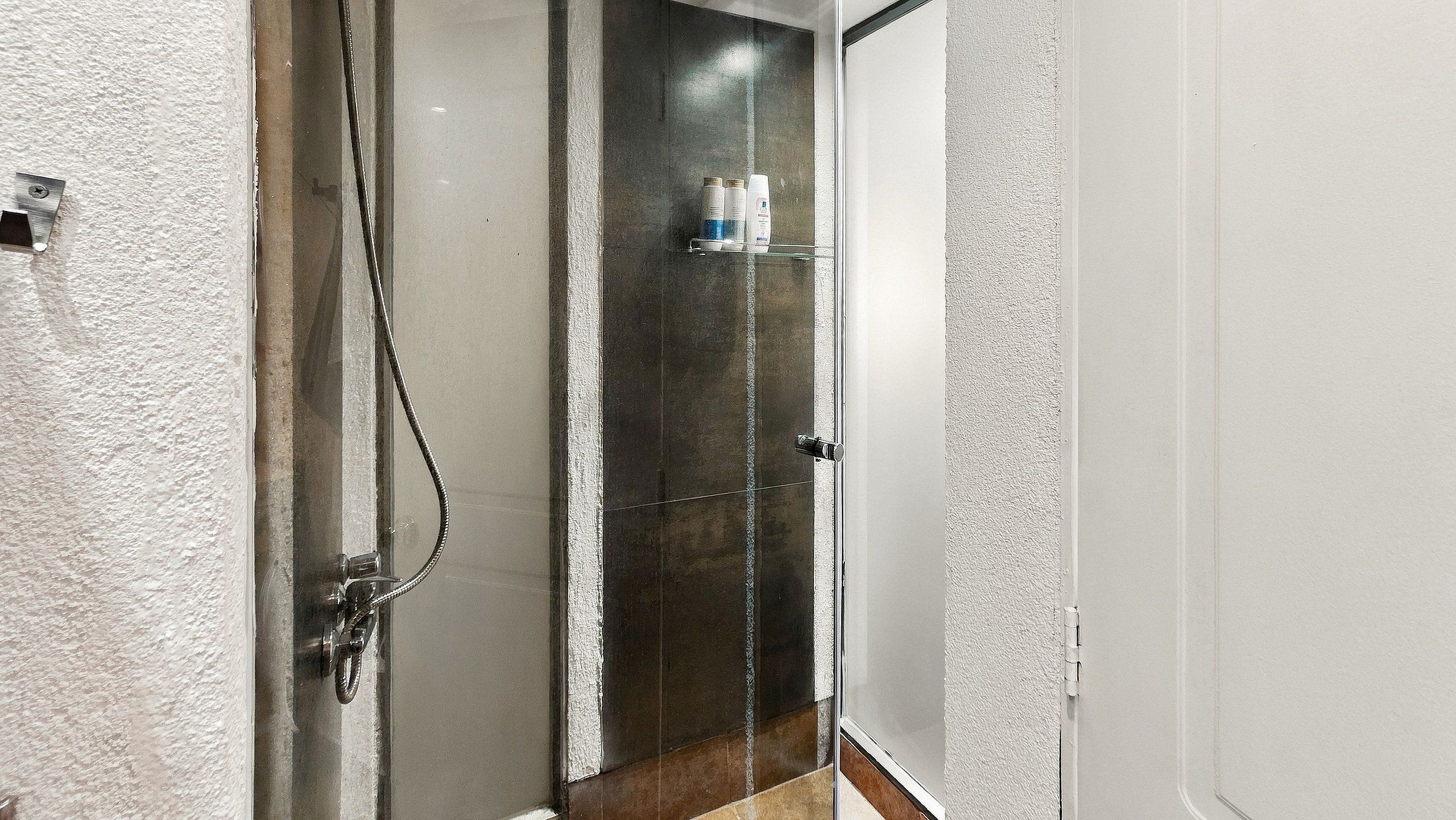 Ducha con puerta de cristal, toallero con artículos de aseo y suelo de madera.