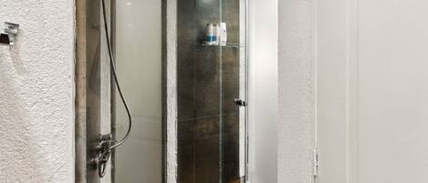 Ducha con puerta de cristal, toallero con artículos de aseo y suelo de madera.
