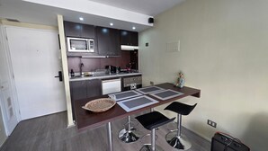 A compact kitchen with a microwave, stove, and sink, a dining table with chairs, and a Buddha statue. - Oceana Suites Providencia (Santiago)