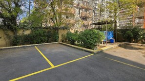 A parking area with yellow lines marking spaces, surrounded by greenery and a building in the background. - Oceana Suites Providencia (Santiago)