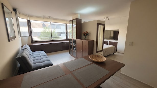 A modern living room with a sofa, a dining table with mats, a cabinet, and a view of the outside. - Oceana Suites Providencia (Santiago)