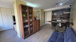 A modern living room with a sofa, a wooden cabinet with glass doors, and a kitchen area with a microwave and stove. - Oceana Suites Providencia (Santiago)
