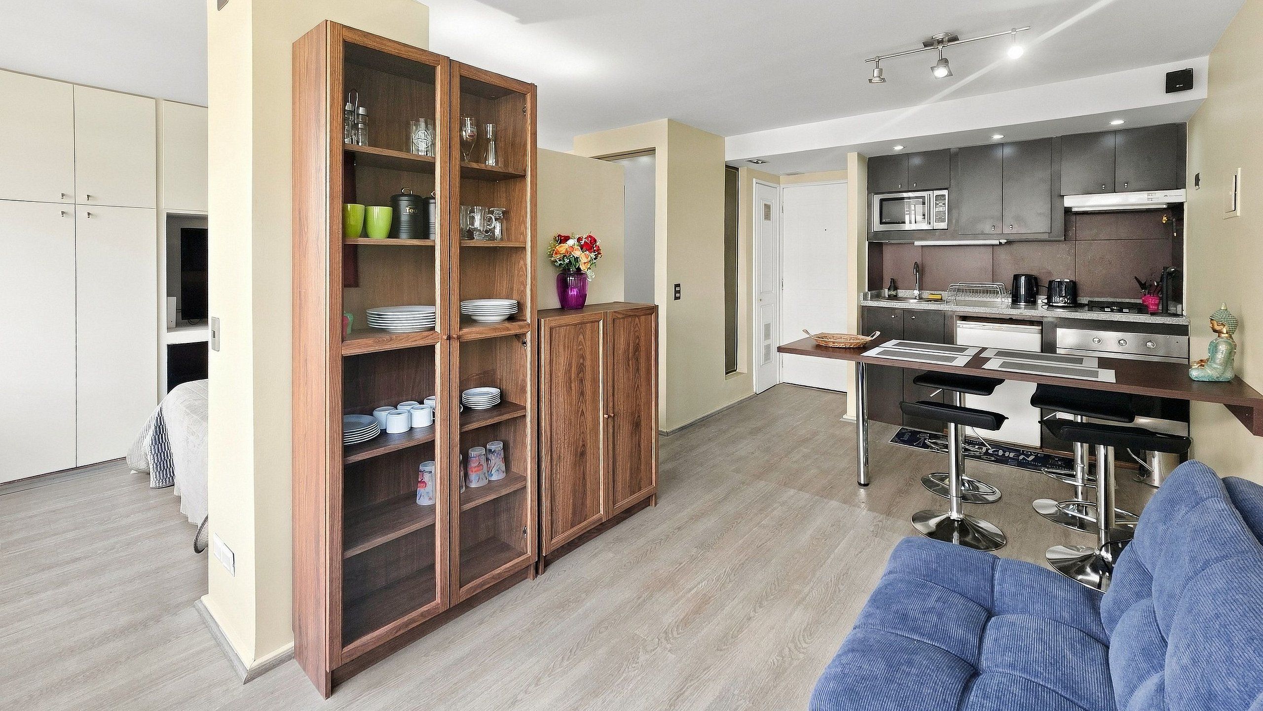 Un espacio habitable compacto con kitchenette, comedor y armario con estantes abiertos.