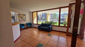 A room with a sofa, two chairs, a window with a view of buildings, and a door with a sign.