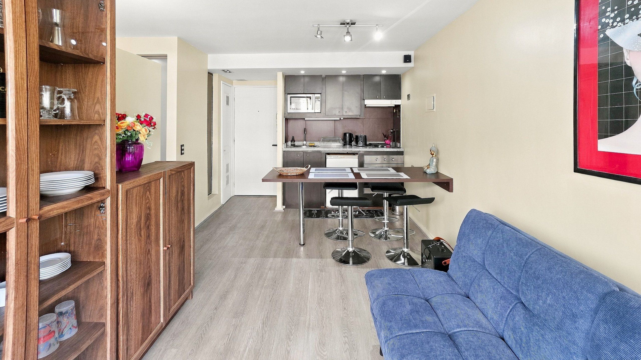 Un espacio habitable compacto con kitchenette, zona de comedor y sala de estar con sofá azul.