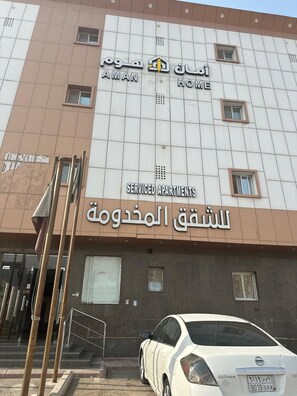 A building with a sign that reads 'AMAN HOME' and 'SERVICED APARTMENTS' in English and Arabic. There is a white car parked in front. - Aman Home 1 for serviced appartments (Riyadh)