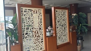 A reception area with a modern ceiling design, wooden reception desk, and potted plants. - Aman Home 1 for serviced appartments (Riyadh)