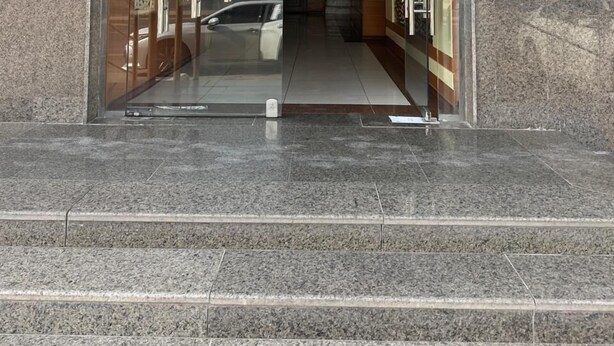 A building entrance with a glass door, a staircase leading up, and a car parked outside. - Aman Home 1 for serviced appartments (Riyadh)