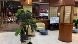 A lobby with a reception desk, a seating area with a sofa and armchairs, a trash bin, and a large pillar with a decorative design. - Aman Home 1 for serviced appartments (Riyadh)
