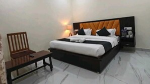 Ein ordentlich eingerichtetes Hotelzimmer mit einem großen Bett, einem Nachttisch, einem Stuhl und einem Beistelltisch mit Lampe.