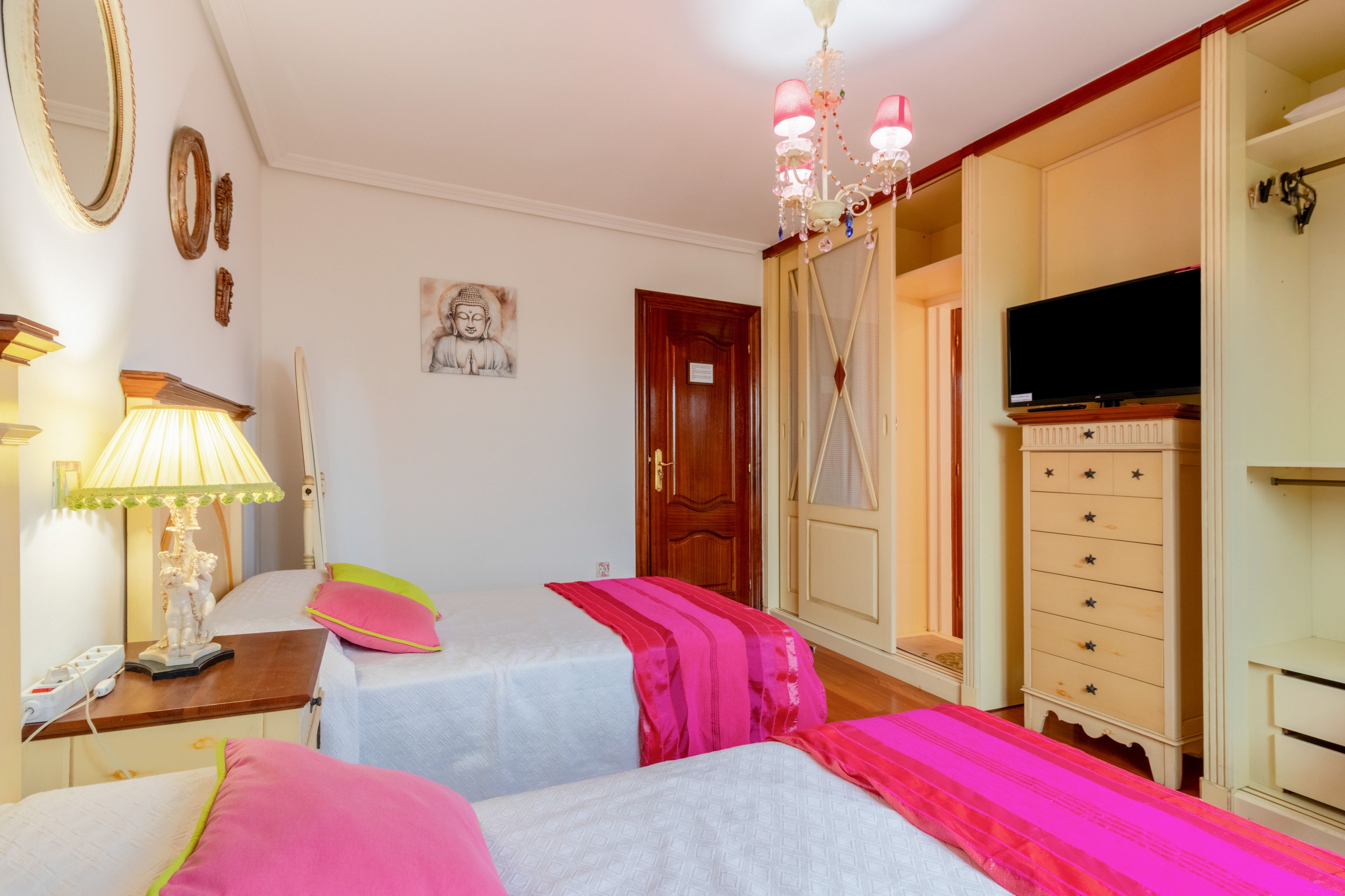 Une chambre avec deux lits, une télévision, une commode et un lustre.