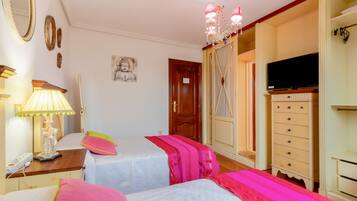 Une chambre avec deux lits, une télévision, une commode et un lustre.