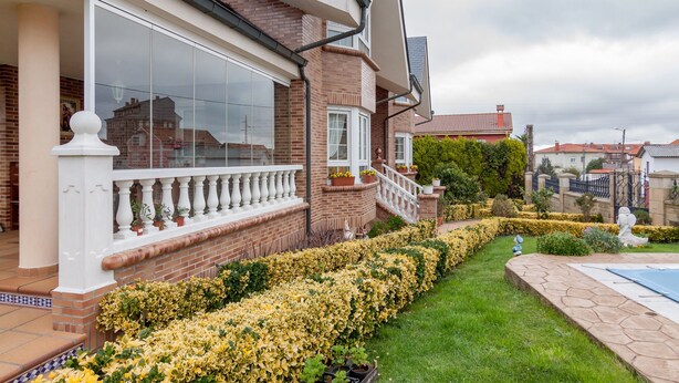 Una casa con fachada de ladrillo, ventanas amplias, un balcón blanco y un jardín cuidado con flores amarillas.