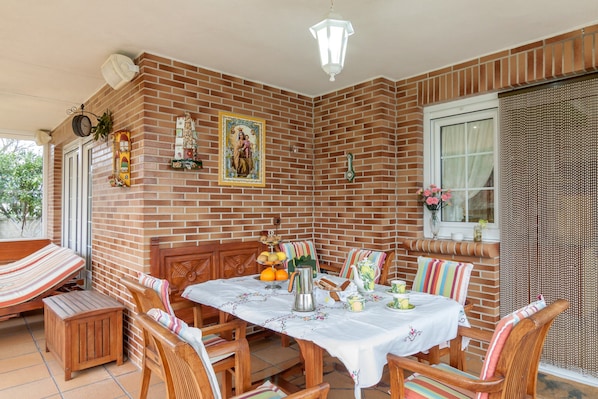 A dining area with a brick wall, wooden furniture, a table with a white tablecloth, and a hanging light fixture.