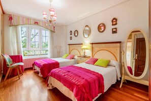 A bedroom with two beds, a window with curtains, a chandelier, and a mirror.