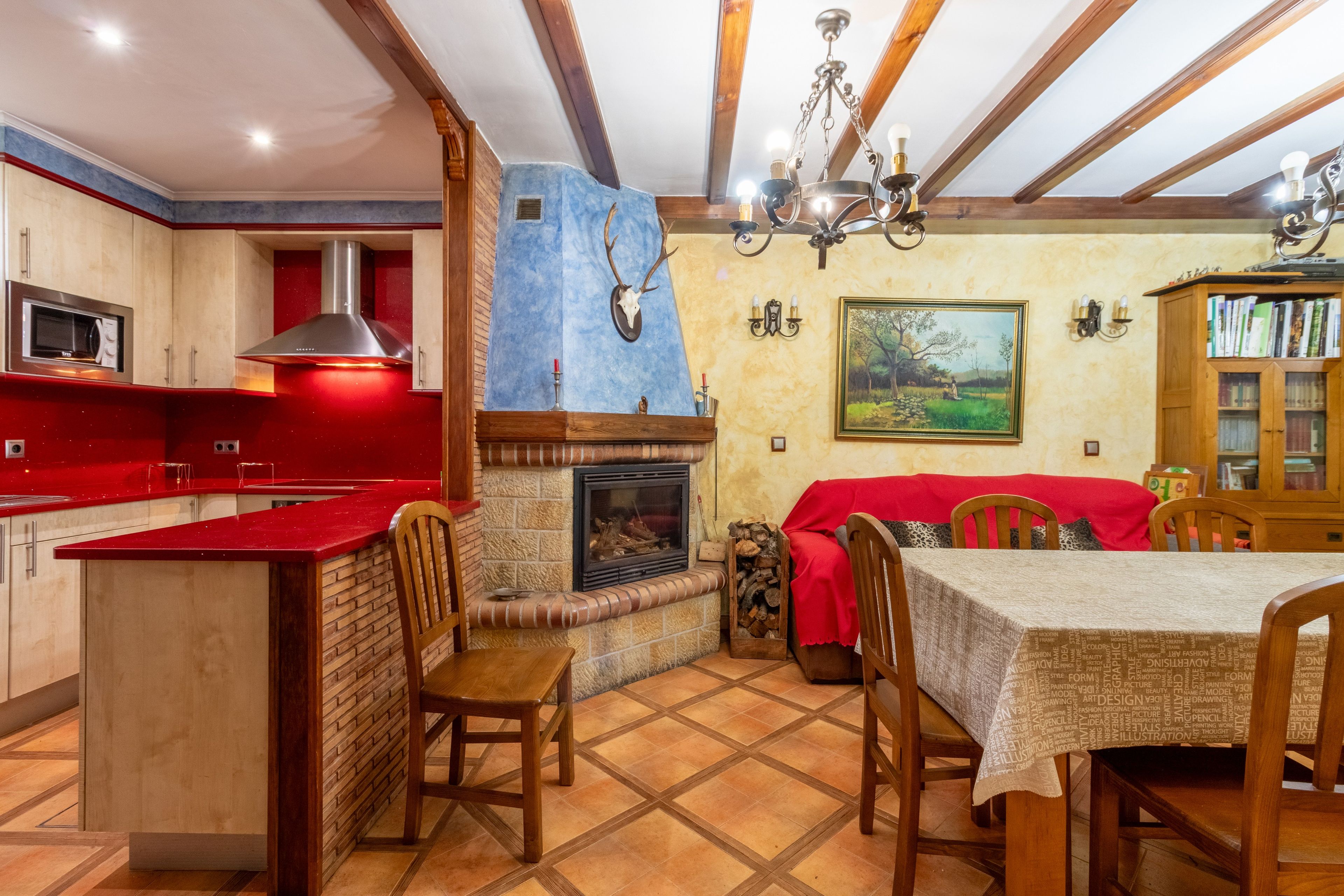 Un coin repas avec une cheminée, des chaises en bois, une table recouverte d’une nappe rouge et une bibliothèque.