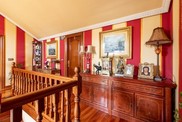 A grand hallway with a wooden staircase, a large wooden cabinet with multiple drawers, and a door marked with the number 5.