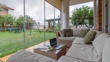 Ein modernes Wohnzimmer mit einer Couch, einem Couchtisch und einem Laptop. Ein Glastür führt zu einem Garten mit einer Schaukel.