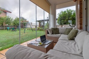 A modern living room with a sofa, a coffee table, and a laptop. There is a glass door leading to a garden with a swing set.