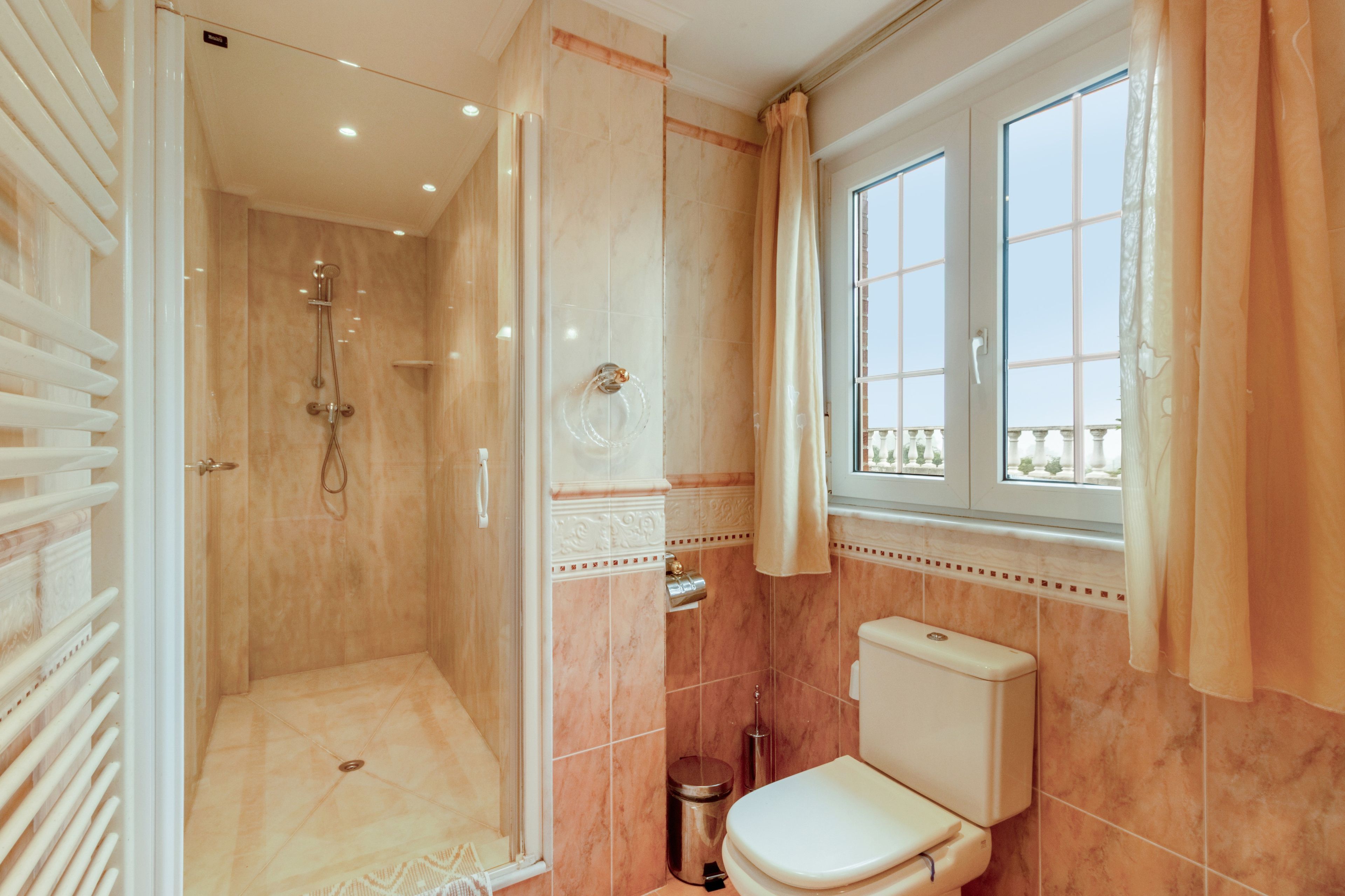Une salle de bain avec douche, toilettes et une fenêtre avec des rideaux.